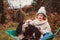 Happy funny child girl riding her dog in wheelbarrow in autumn garden, candid outdoor capture