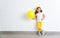 Happy funny child girl with yellow balloon near an empty wall