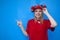Happy funny girl fan in red uniform shows fingers on a place for text and smiles, joyful cheerleader on a blue background