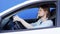 Happy funny man is listening to music and dancing in the car. Young driver is sitting in white car with blue background