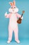 Happy funny musician kid boy or girl guitarist is playing music by ukulele or Hawaiian guitar. Easter bunny or rabbit or