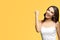 Happy gesturing beautiful woman, raising hand up with clenching fist. isolated over yellow color background. Excited brunette girl