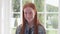 Happy ginger girl with freckles smiling against white window