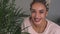 Happy girl with beautiful eyes smiling near leaves of plant in room