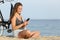 Happy girl with bike using phone sitting on the beach