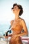 Happy girl in bikini using hose pipe on beach. Portrait of lady in beige swimsuit rinsing beach sand off her body on