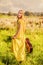 Happy girl in bohemian style yellow dress with guitar on the field turned back