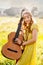 Happy girl in bohemian style yellow dress with guitar on the field turned back at sunset
