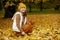 Happy girl in brown sweater and hat collecting autumn leaves