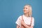 Happy girl in cute clothes standing against the background of a blue wall, showing her finger aside and smiling. Teen girl looks