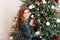 Happy girl decorate the Christmas tree. Portrait smilling redhead little girl near Xmas tree. Christmas celebration. Child decorat