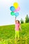 Happy girl with flying balloons stands on grass