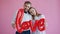 Happy girl and guy standing beside holding English word Love on pink background