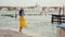Happy girl in hat, yellow skirt runs barefoot, whirls, has fun on pier in Venice