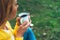 Happy girl holding in hands cup of hot tea on green grass in outdoors nature park, beautiful woman hipster enjoy drinking cup