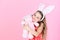 Happy girl hugging rabbit toy on pink background