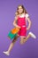 Happy girl jump with shopping bag on violet background. Little child smile with paper bag. Kid shopper in fashion