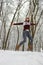 Happy girl in knitted cozy wear jumping in snowy winter forest. Christmas background. Attractive winter landscape. Jumping woman.