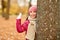 Happy girl peeking out tree in autumn park