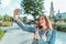 Happy girl pictures herself on phone, selfie on smartphone, denim jacket, summer in city park. Emotions of happiness