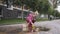 Happy girl in pink clothes playing with paper boats next to puddle. Wide shot portrait of positive little Caucasian