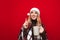 Happy girl in plaid and christmas hat stands on red background with cup of hot drink in her hand and has ideas, looks away and