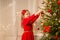 Happy girl in red dress decorating christmas tree