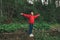 A happy girl in a red raincoat stands on a log over a mountain stream and rejoices with her hands raised. Joyful woman hiking