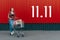 Happy girl with shopping cart on red wall shop background with 11.11 day number. Young woman pushing a shopping cart