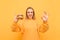 Happy girl shows an OK sign and looks in camera and holds a burger in his hand, isolated on a yellow background. Hungry girl eats