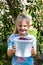 A happy girl smiles and holds a bucket of ripe cherry berries on a sunny summer day in the village.