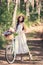 happy girl in straw hat and white dress posing with bike and flowers