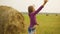 Happy girl stretching hand to sky on hay stack background. Teenager girl raising hands enjoying nature on harvesting