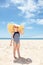 Happy girl in striped swimsuit and big straw hat on white beach