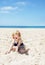 Happy girl in striped swimsuit playing with sand on white beach