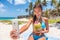 Happy girl taking selfie on summer beach vacation. Cute Asian multiracial bikini woman drinking fresh coconut water