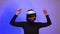 Happy girl in virtual reality helmet raises her hands up, dances, purple neon light, full hd. The concept of the virtual