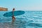 Happy girl walk in ocean with surfboard. Calm sea view on summer day. Idea of surf sport, beach day and summer holidays