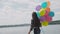 Happy girl walks and poses with colourful balloons on the shore of the lake