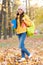 Happy girl wear earphones in autumn park with book and backpack, school education