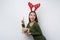 Happy girl wearing Christmas deer horns holding a gift box pointing finger up