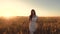 Happy girl in white dress walks field with wheat in rays of beautiful sunset. girl touches the ears of ripe wheat. Slow