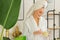 A happy girl in a white robe and with a towel on her head in the bathroom enjoying life holds a jar of cream in her hand