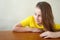 Happy girl in yellow clothes sitting at wooden table and looking thoughtfully away