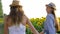 Happy girlfriends in straw hats walk by hands on field with yellow sunflower outdoors
