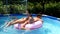 Happy girls have fun floating together on swim ring in outdoor swimming pool, summer