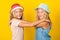 Happy girls wearing summer hat, posing over yellow background. Pretty sisters twins hugging and smiling. Summer fashion. Happy