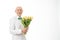 Happy, glad, cheerful, joyful smiling old man in white shirt, senior holds bouquet of yellow flowers in hands and