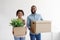 Happy glad millennial african american male and female carry cardboard boxes with plant and relocate to new apartment