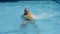 Happy goofy young woman swirling in blue water of swimming pool holding a yellow inflatable toy. Playful girl rotating